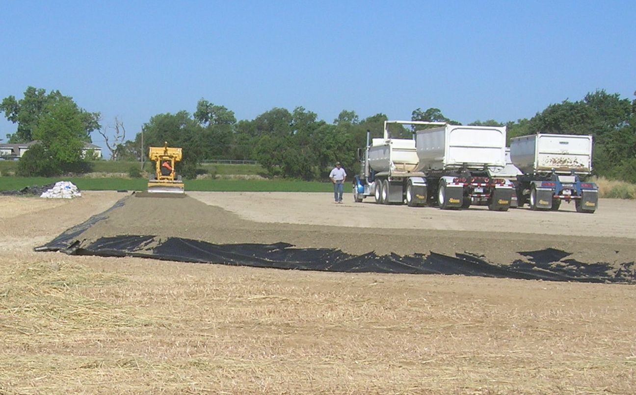 distant shot of a large piece of machinery leveling dirt and a man standing next to a few white dirt trucks