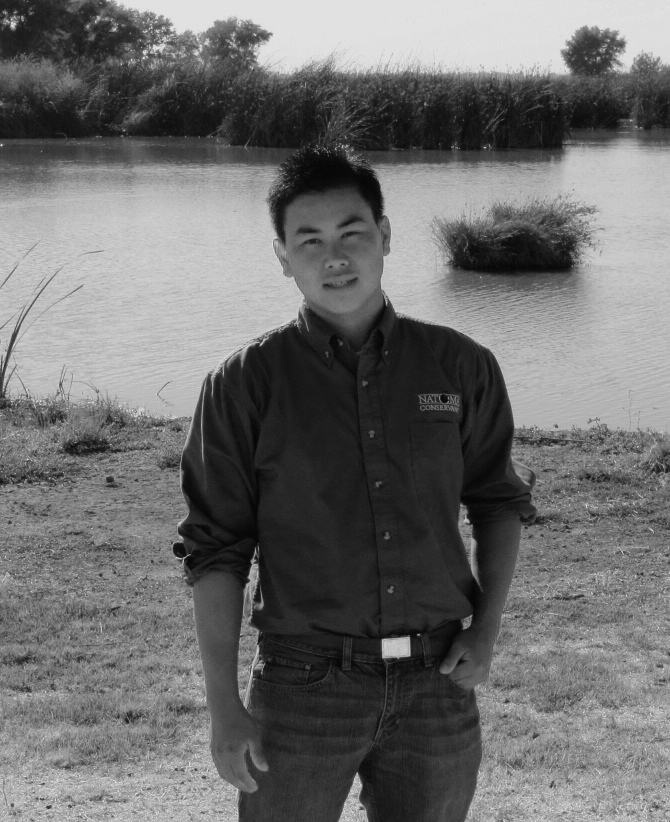 black and white photo of Jeremy Lor, Field Services Assistant, standing near a marsh in the background