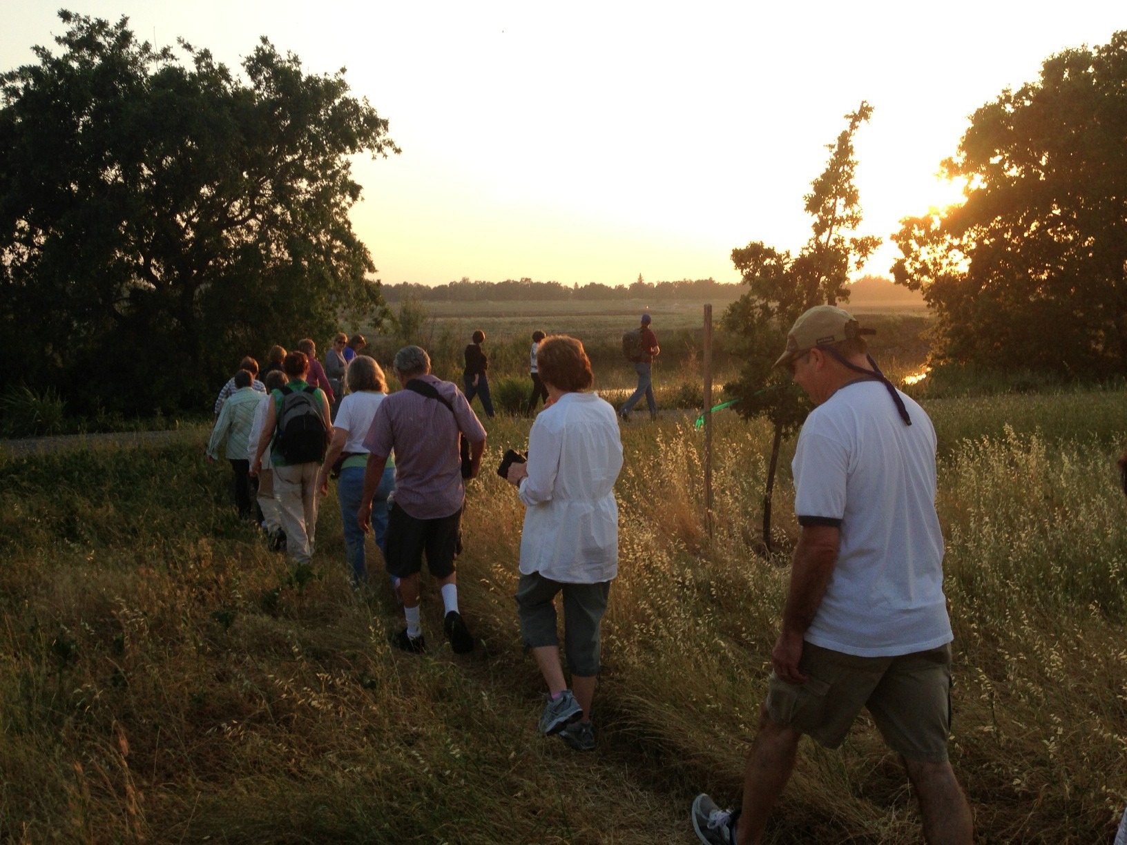 rear angle of people walking single-file along a dirt trail at the Conservancy preserves